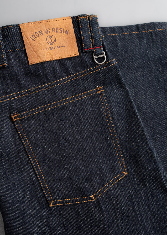 Dark denim jeans with a leather "Iron and Resin" patch, visible back pocket, and belt loop detail.