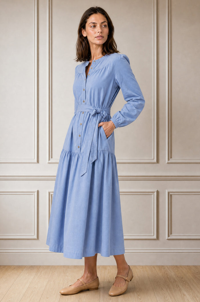 Model wearing the Aspiga Baby Cord Midi Dress in Ice Blue, a light blue corduroy belted shirt dress with long sleeves and a collar, alternate view