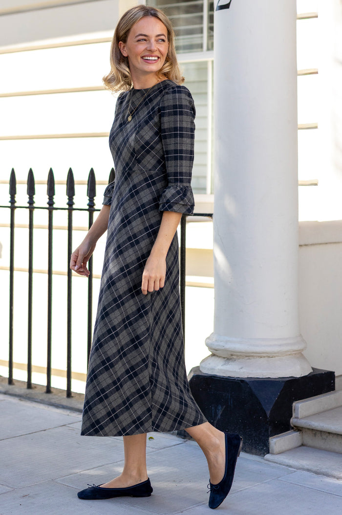 Model wearing the Aspiga Elizabeth Check Dress in Blue/Grey with navy ballet flats, full-length side view walking, smiling
