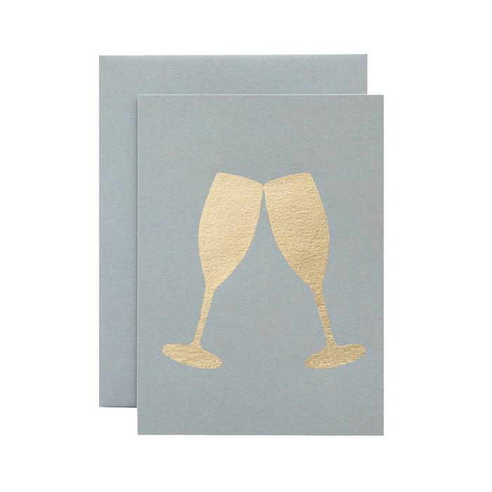 A light gray card with the silhouette of two champagne glasses touching at the rim in solid gold leaf.