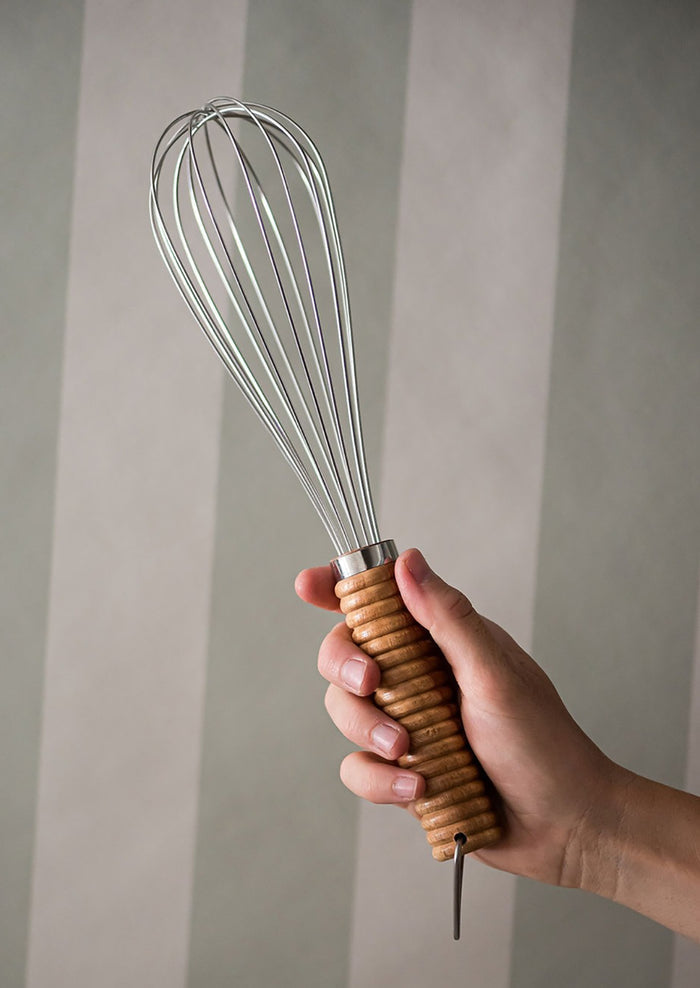 A stainless steel whisk with ribbed wooden handle.