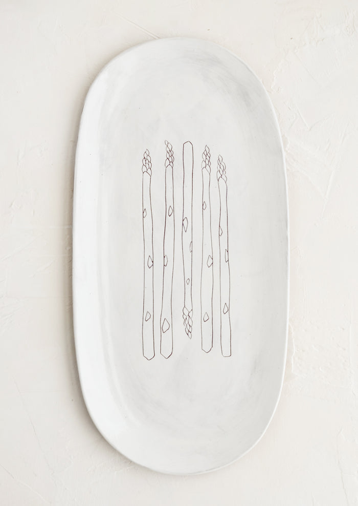 An oval shaped ceramic serving platter with hand drawn asparagus illustration at center.