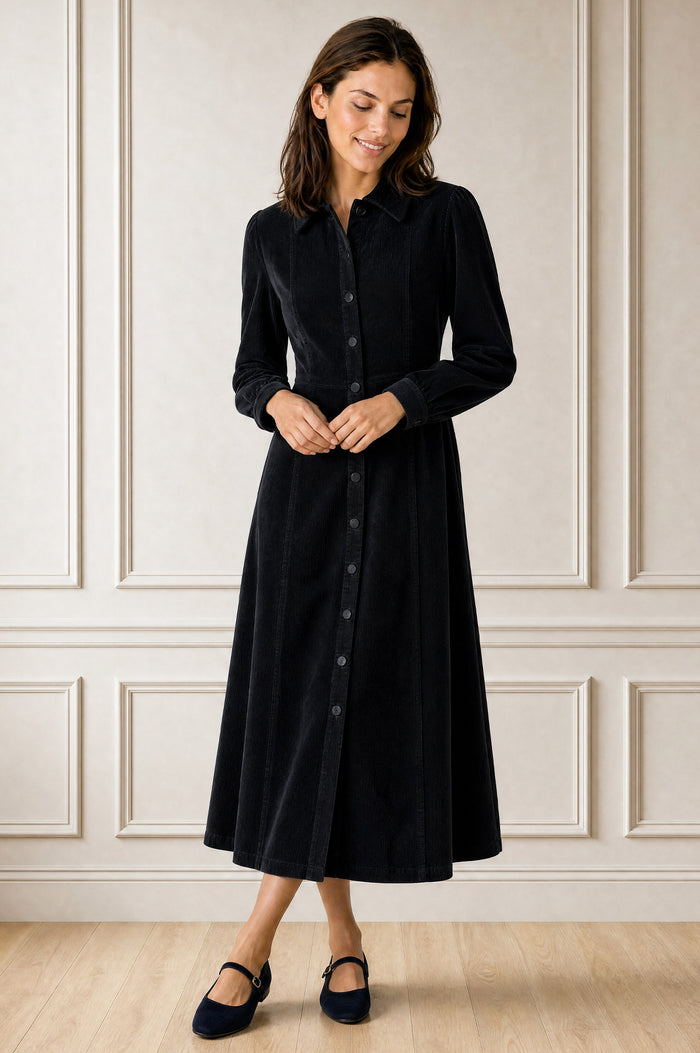 Model wearing the Aspiga A-Line Cord Dress in Navy, a corduroy button-front shirt dress with a collar, long sleeves and a tie waist, front view
