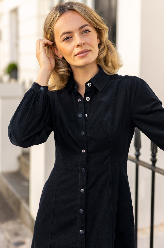 Close-up of a model wearing the Aspiga A-Line Baby Cord Dress in Navy, a corduroy button-front shirt dress with a collar and puff-shoulder long sleeves
