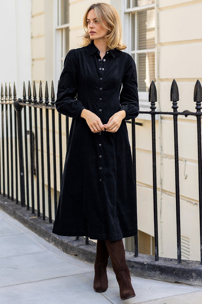 Model wearing the Aspiga A-Line Baby Cord Dress in Navy, a corduroy button-front shirt dress with a collar and puff-shoulder long sleeves, full-length front view