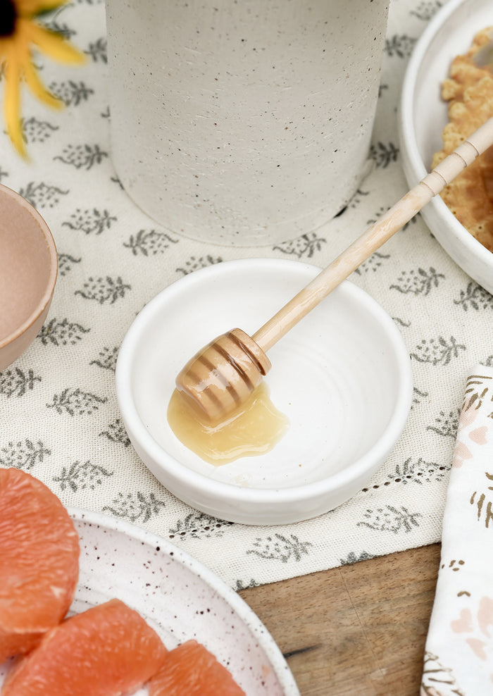 A small white ceramic bowl with honey dipper.