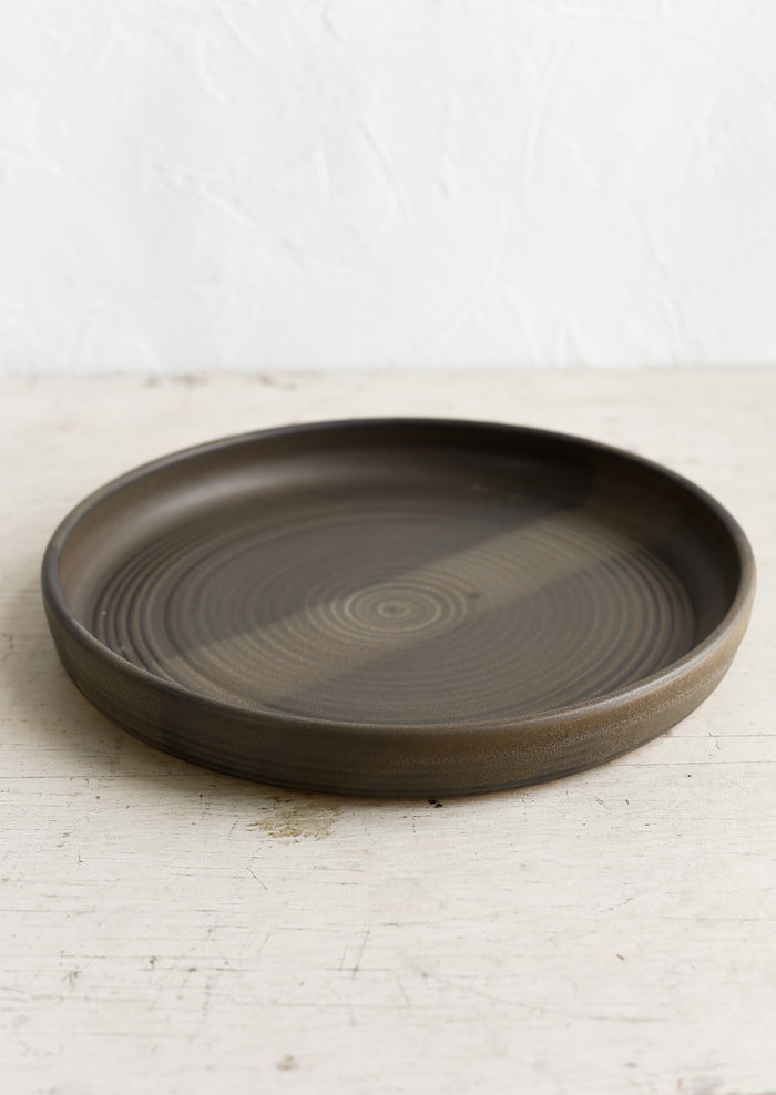 A shallow serving plate in matte dark brown.
