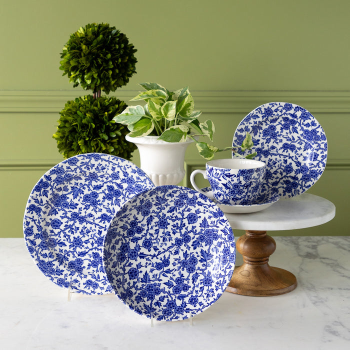 Burleigh Blue Arden Dinnerware displayed on a marble table with plants behind them.