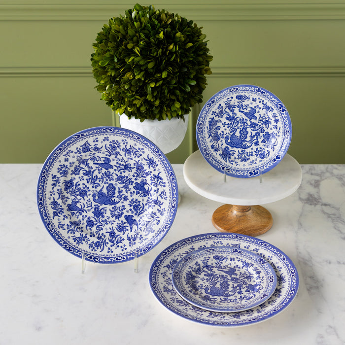 Burleigh Blue Regal Peacock Dinnerware propped on stands in front of a topiary plant.