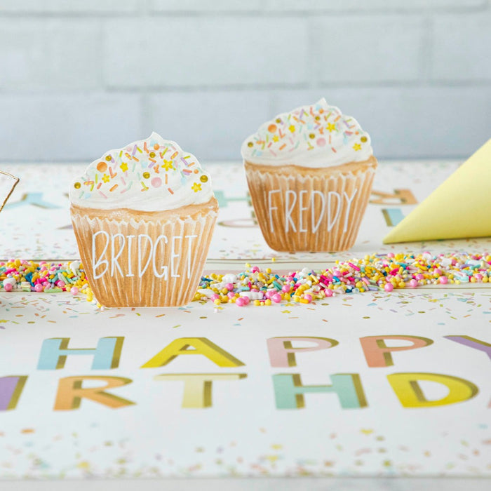 A life-sized Hester & Cook Cupcake Place Card sits atop a party place setting accessory, surrounded by confetti and a birthday banner.
