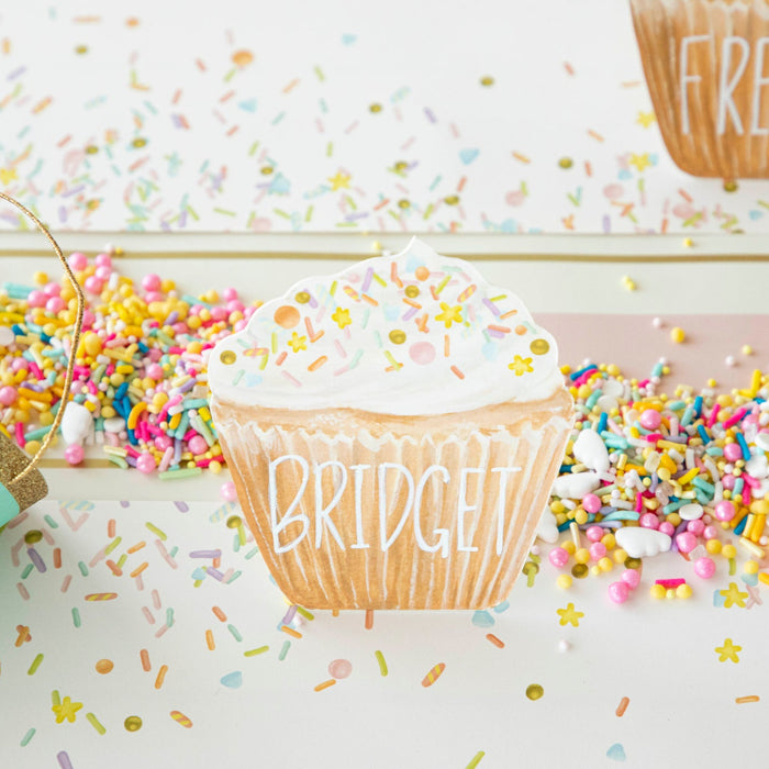 Cupcake Place Card with "Bridget" written on the wrapper part, on a table surrounded by sprinkles.