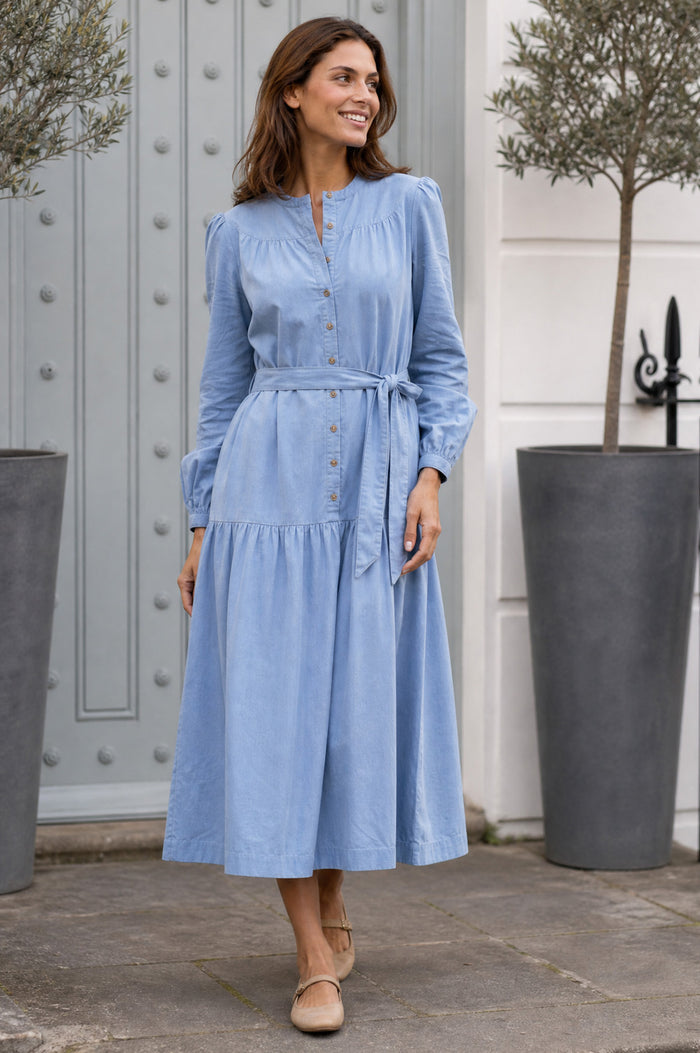Model wearing the Aspiga Baby Cord Midi Dress in Ice Blue, a light blue corduroy belted shirt dress with long sleeves and a collar, front view