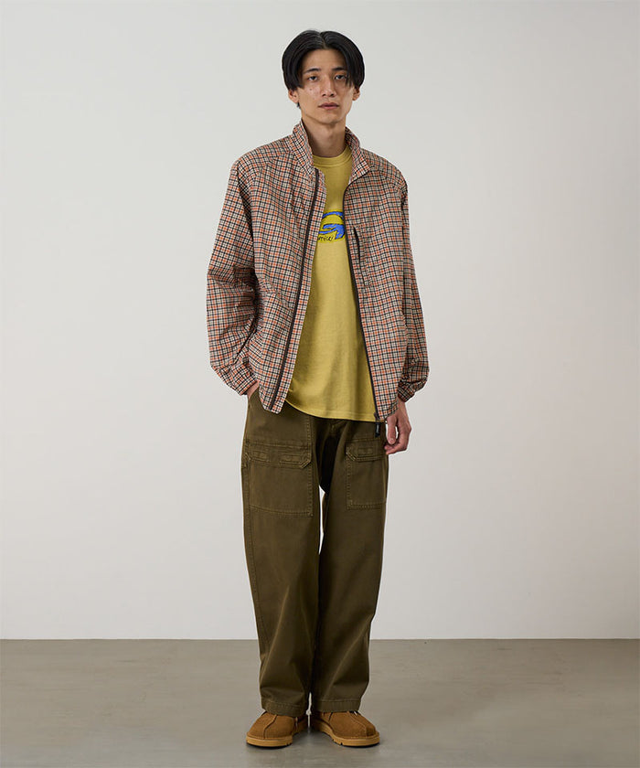 Model wearing bark pigment Gramicci EQT Pant and a plaid jacket on a light-tone background.