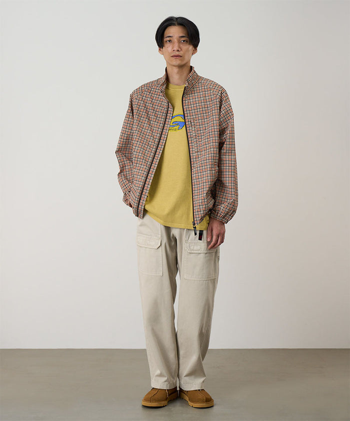 Model wearing sand pigment Gramicci EQT Pant and a plaid jacket on a light-tone background.