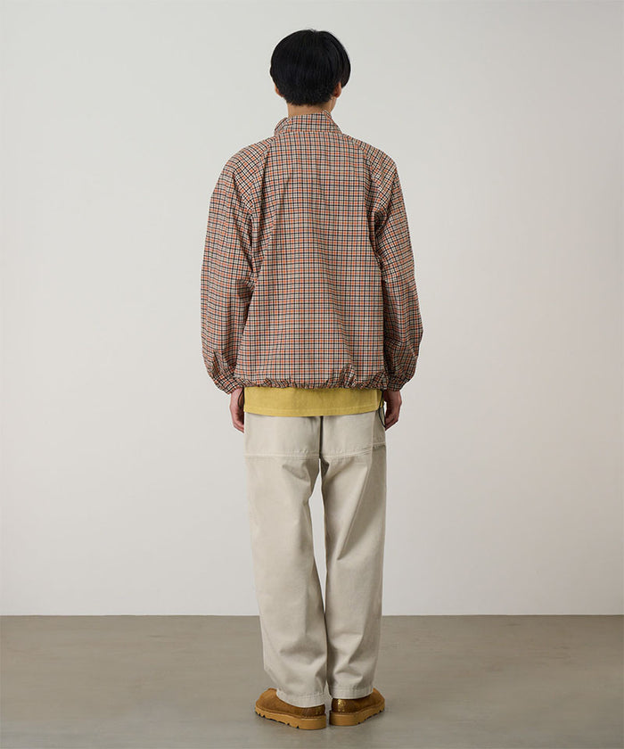 Back view of a model wearing sand pigment Gramicci EQT Pant and a plaid jacket on a light-tone background.