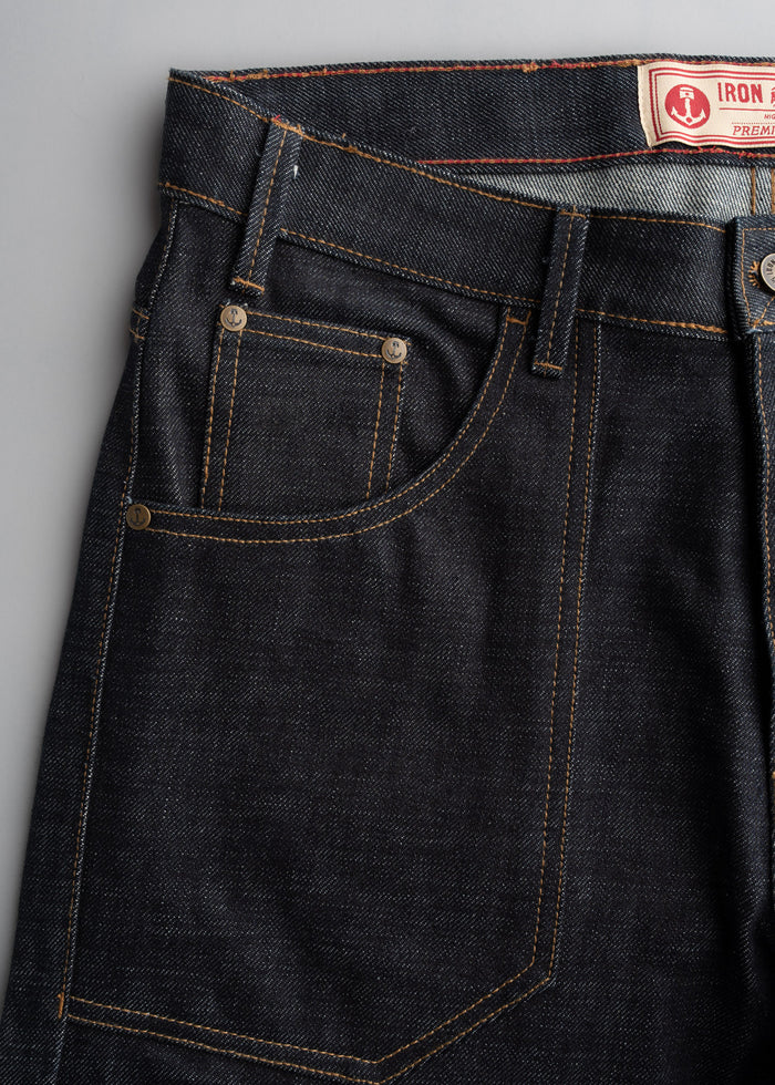 Close-up of dark denim jeans with orange stitching and a branded label on the waistband, showcasing pocket details.