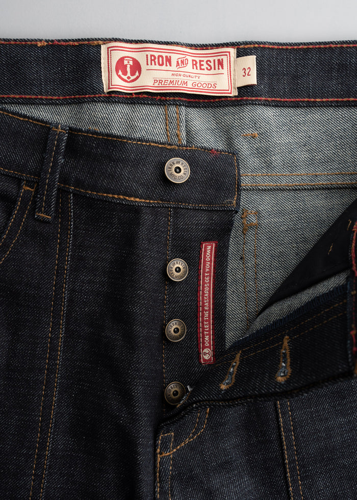 Close-up of Iron and Resin jeans with button fly, visible label, and red stitching detail, showcasing premium denim craftsmanship.