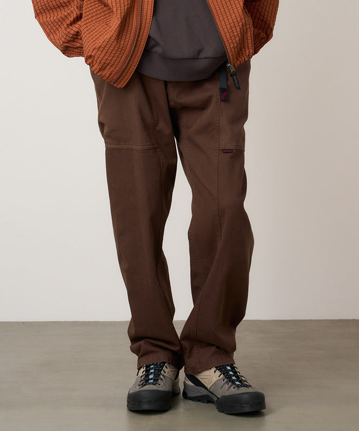Model wearing tobacco colored Gramicci Gadget Pant and a orange jacket on a light-tone background.