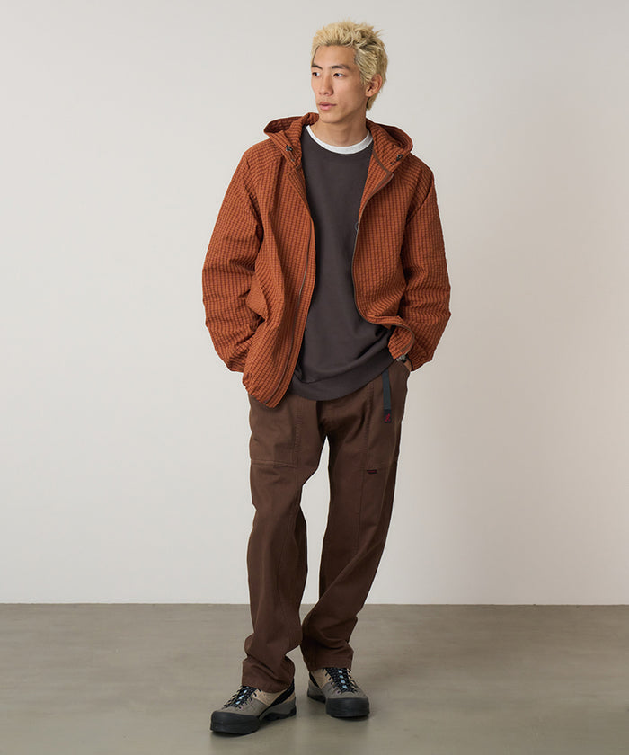 Model wearing tobacco colored Gramicci Gadget Pant and a orange jacket on a light-tone background.