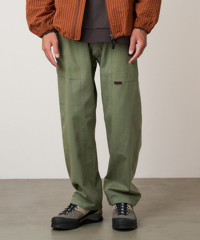 Model wearing sage colored Gramicci Gadget Pant and a orange jacket on a light-tone background.