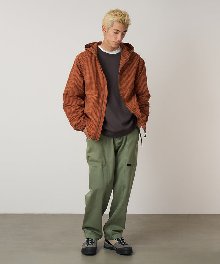 Model wearing sage colored Gramicci Gadget Pant and a orange jacket on a light-tone background.