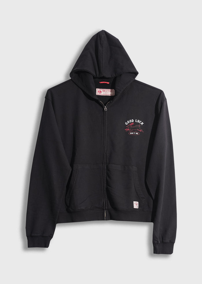 Black zip-up hoodie with "Good Luck" text and graphic on chest, featuring front pockets and a hood, displayed on a plain background.