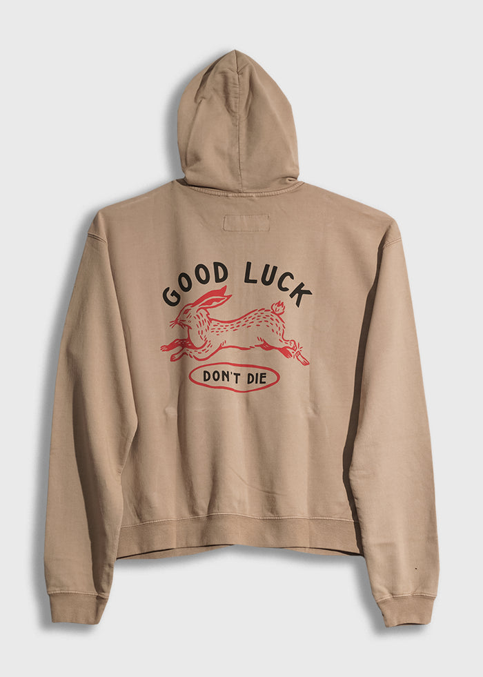 Beige hoodie with "Good Luck Don't Die" and a red rabbit design on the back, conveying a playful and bold message.