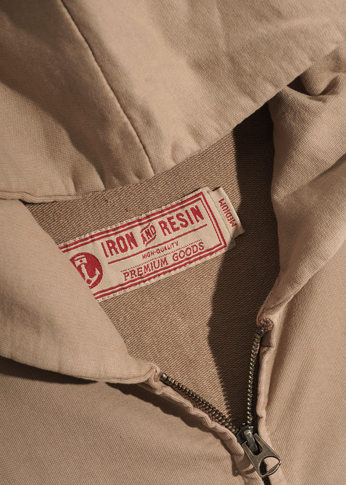 Close-up of a beige jacket with a visible Iron and Resin label, highlighting the zipper and fabric texture.