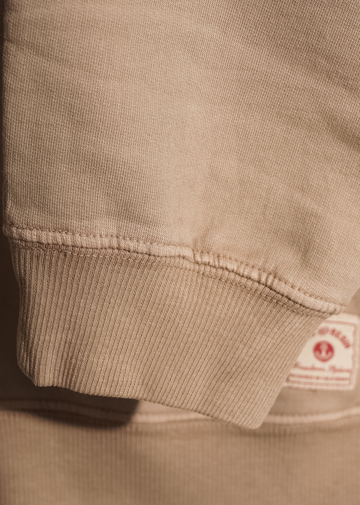 Close-up of a beige sweatshirt sleeve with ribbed cuff, showcasing texture and a visible label in the background.