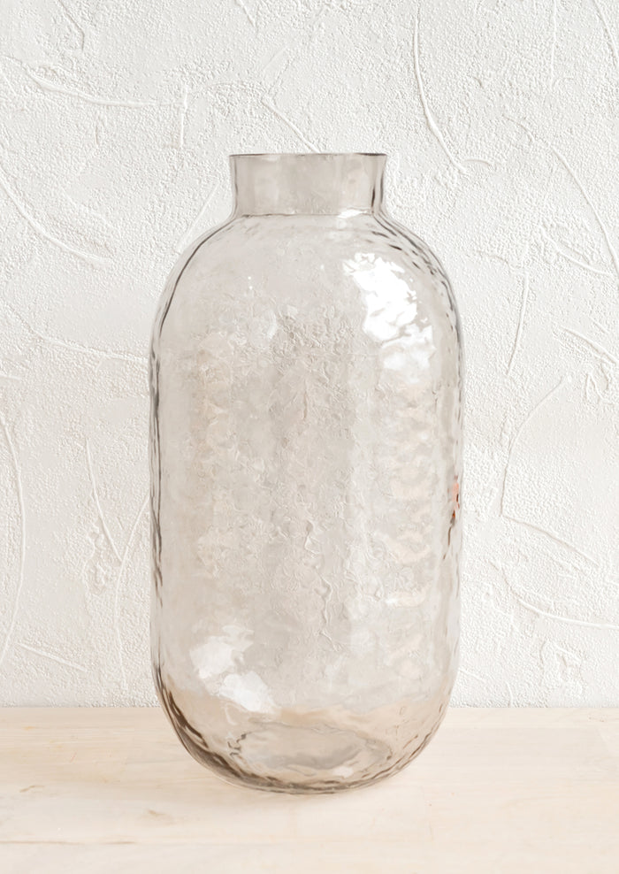 A tall glass vase with hammered texture in pale grey.