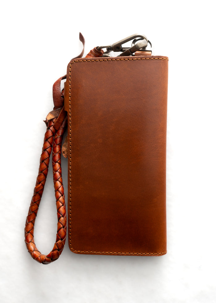 Brown leather wallet with braided strap and metal clasp on white background, showcasing craftsmanship and style.