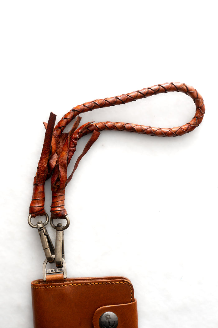 Brown leather wallet with braided strap and metal clasps on a white background, showcasing craftsmanship and style.