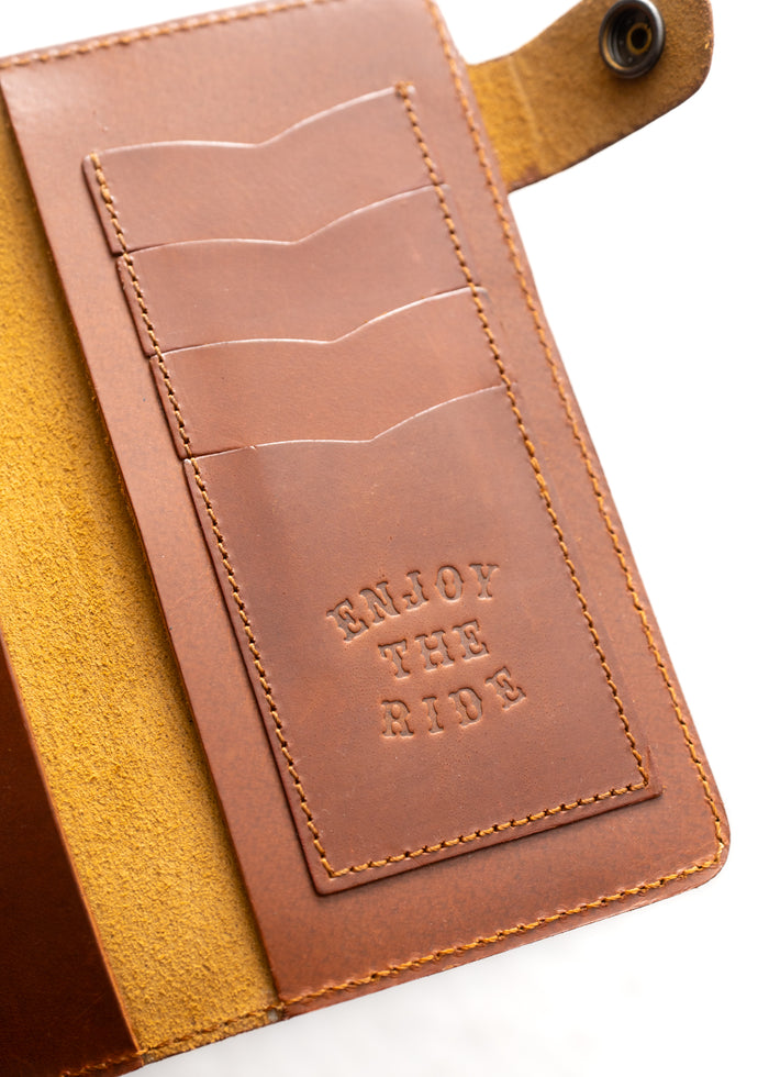 Brown leather wallet with card slots and "ENJOY THE RIDE" embossed, showcasing craftsmanship and style.