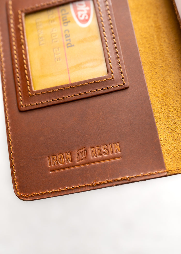 Brown leather wallet with "Iron and Resin" embossed, displaying a club card through a clear window.