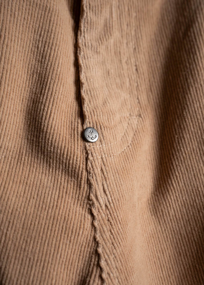 Close-up of a brown corduroy fabric with a visible seam and a small metal button featuring a smiley face design.