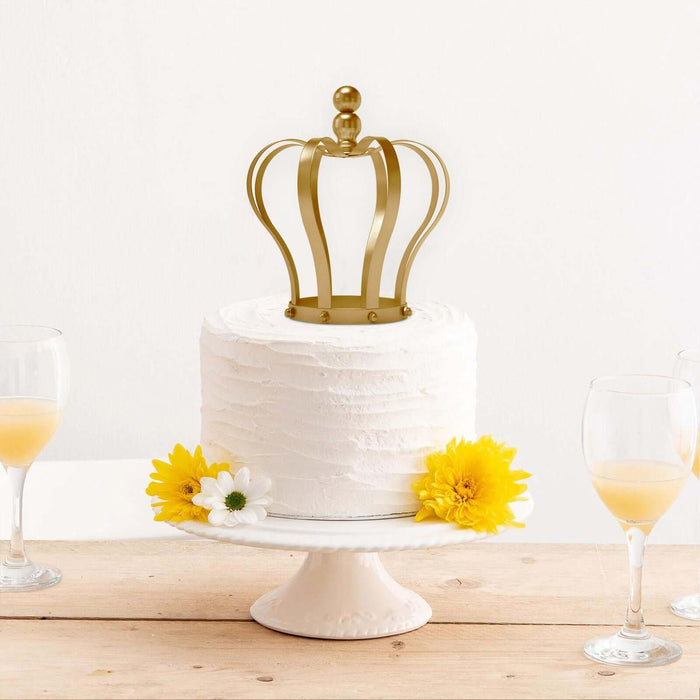 White frosted cake with a golden crown topper and yellow flowers on a cake stand.