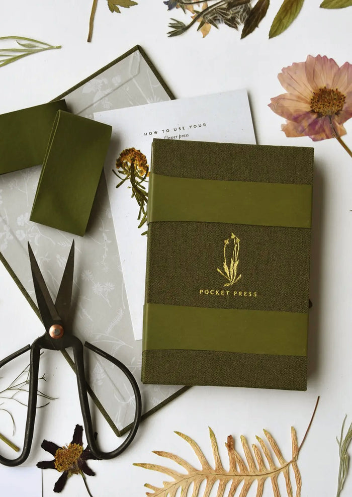 A green linen covered pocket-sized flower press booklet.