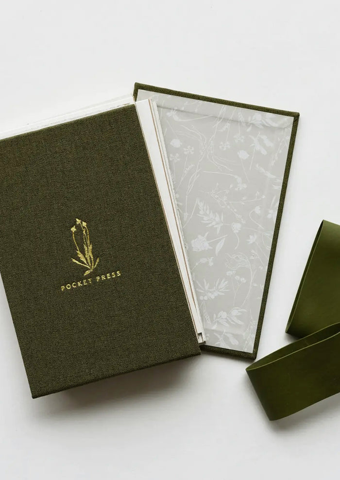 A green linen covered pocket-sized flower press booklet.
