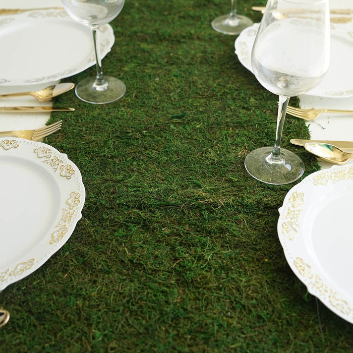 Elegant dining setup with ornate plates and crystal glasses on a moss green table setting.