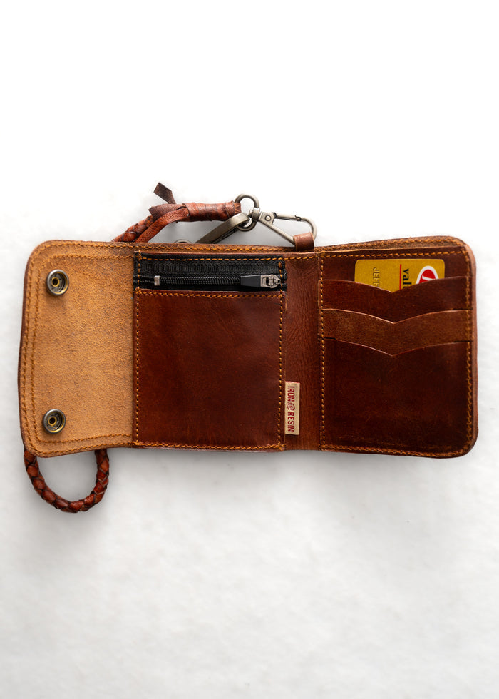 Open brown leather wallet with a braided strap, card slots, and a zipper pocket, displaying a card inside against a white background.