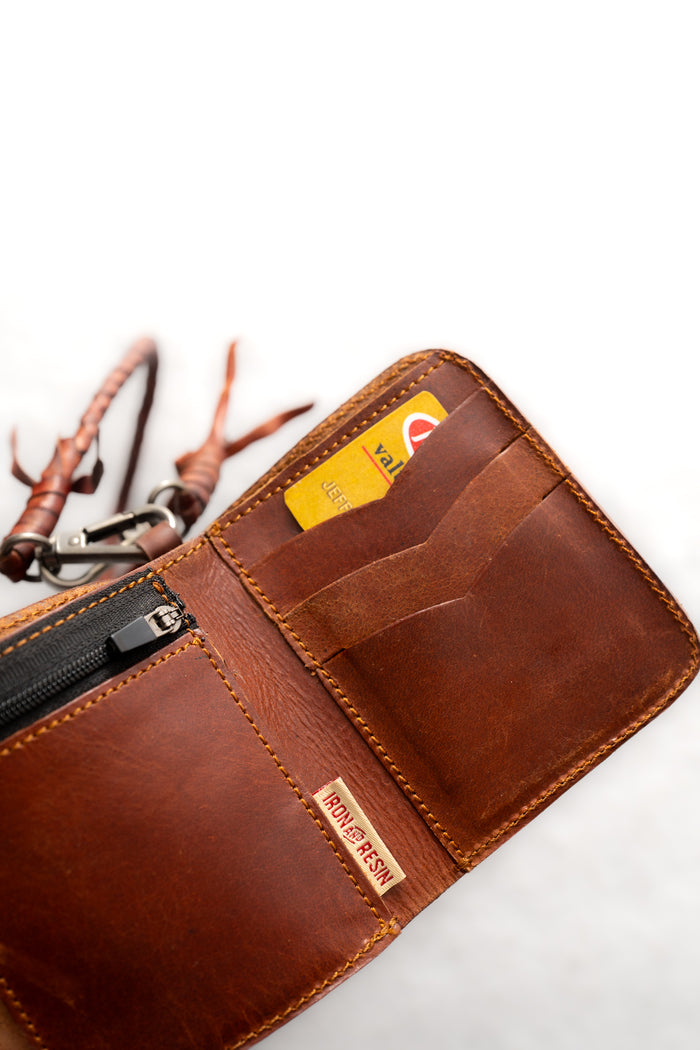 Open brown leather wallet with visible credit card and zipper pocket, labeled "Iron and Resin," on a light background.