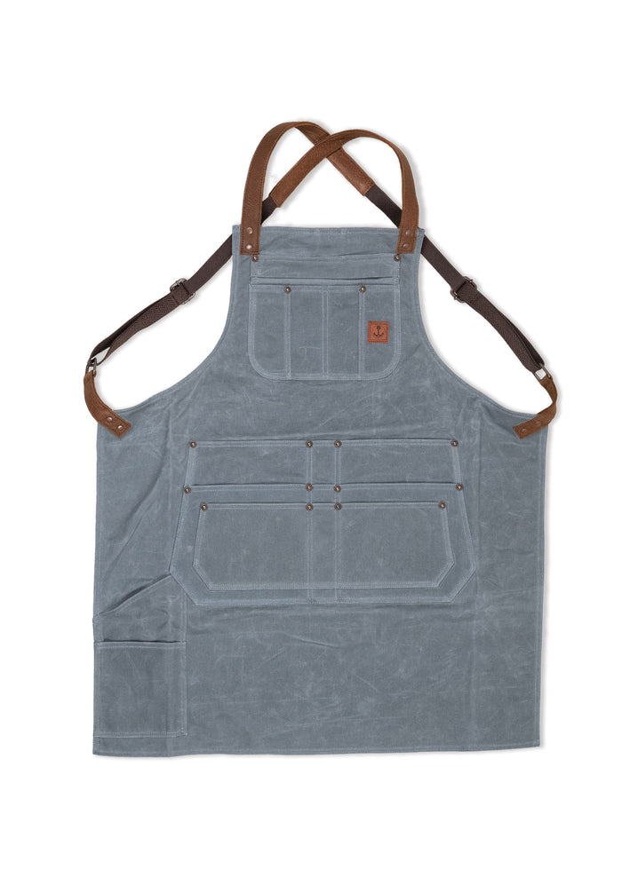 Gray canvas apron with brown leather straps, multiple pockets, and a small anchor logo on the chest. Ideal for work or craft.