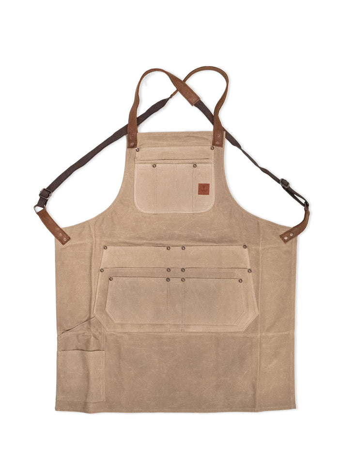 Tan canvas apron with brown leather straps and multiple pockets, designed for utility and style in kitchen or workshop settings.