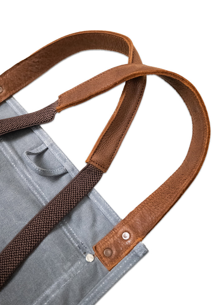 Gray canvas tote bag with brown leather handles and metal rivets, showcasing a durable and stylish design.