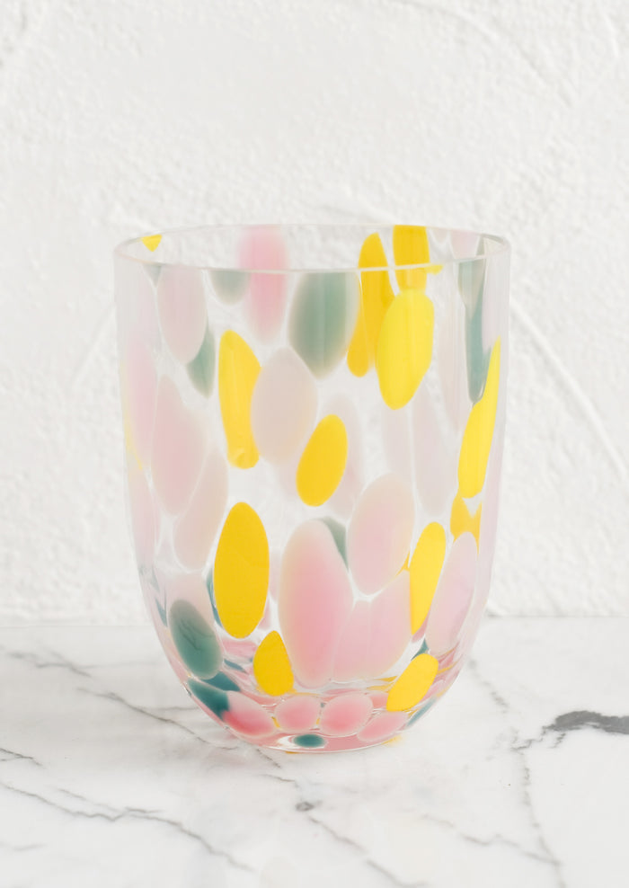 A handmade speckled glass juice cup with teal, yellow and pink spots.
