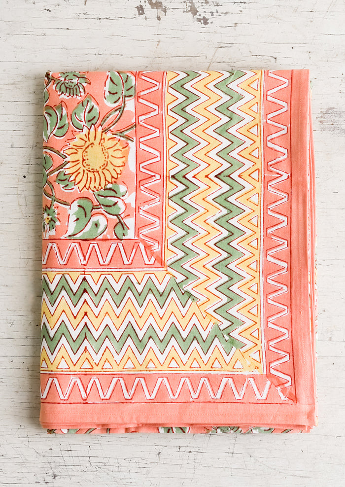 A block printed tablecloth in peach, mint and yellow sunflower pattern with zigzag border.