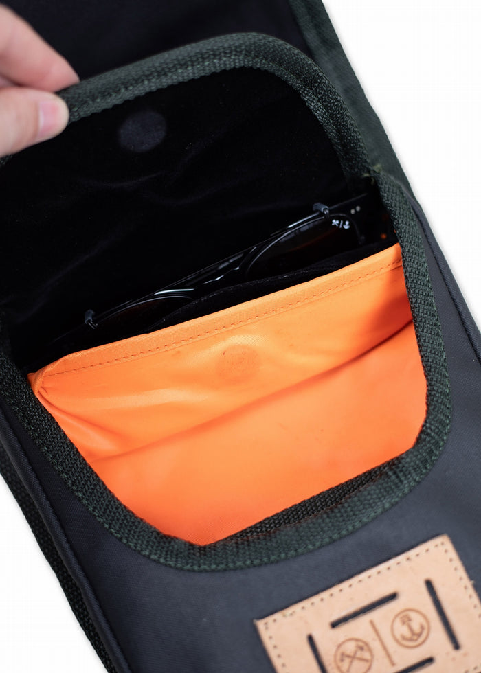 Open black bag with orange lining, holding sunglasses. A hand grips the top, revealing a leather patch with icons on the front.