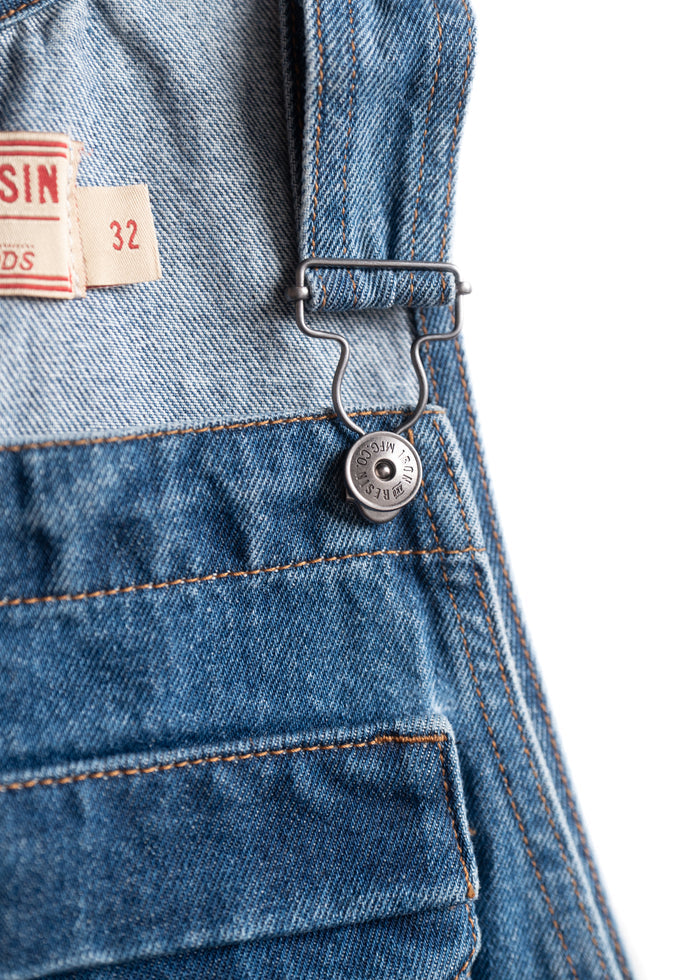 Close-up of blue denim overalls with a metal button and size tag reading "32" on a white background.