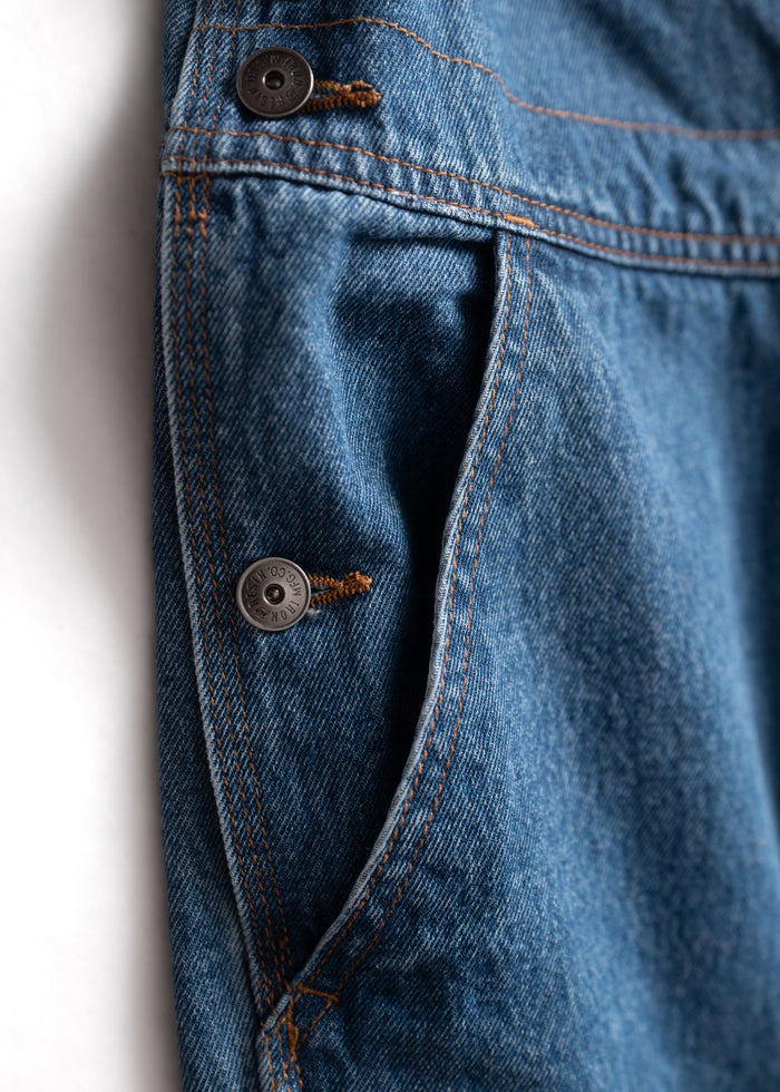 Close-up of blue denim jeans pocket with visible stitching and a metal button, highlighting texture and craftsmanship.