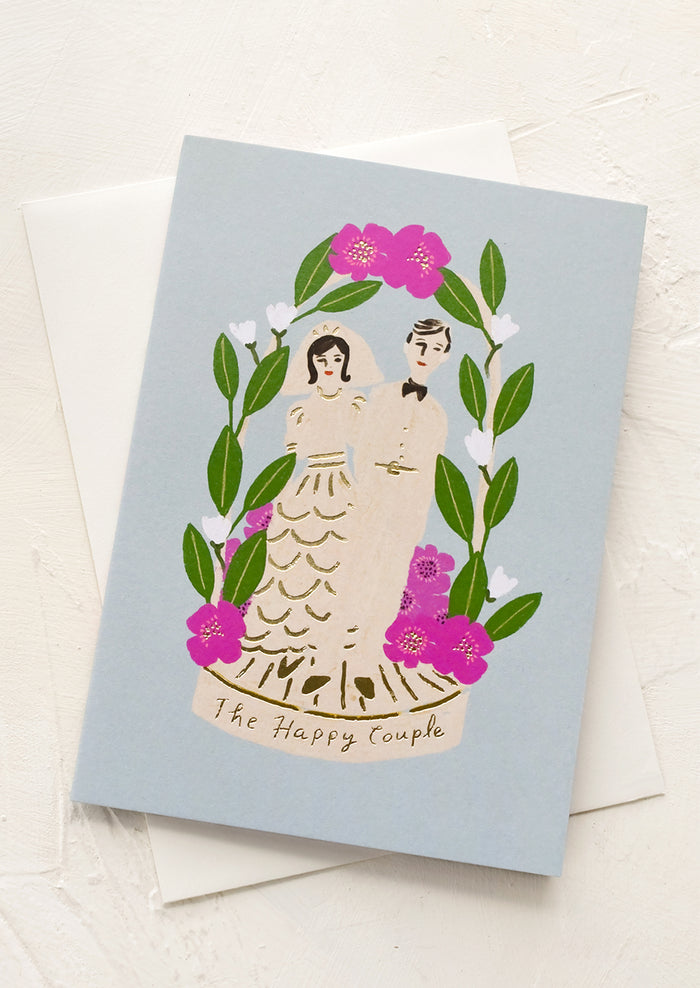 A blue greeting card with bride and groom, text reads "The happy couple".